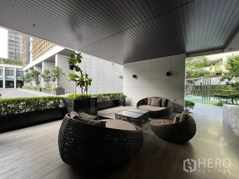Condominium for sale - Covered outdoor seating area with round rattan sofas beside landscaped grounds and pool.