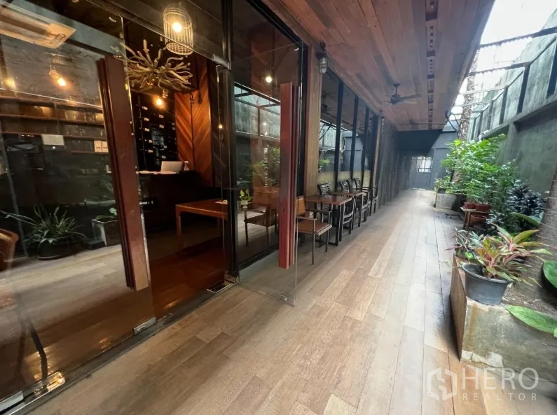 Retail Space for rent in Watthana, Bangkok - Covered patio walkway with glass storefront, potted plants, and wood-look flooring.