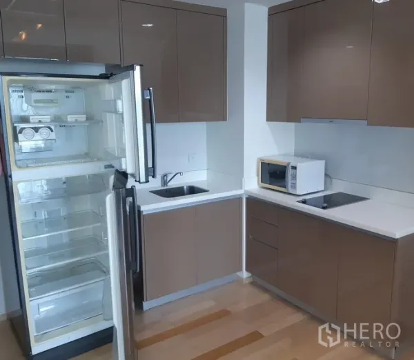 Condominium for rent in Khlong Toei, Bangkok - Modern L-shaped condo kitchen with glossy cabinets, open refrigerator, sink and electric hob in Phra Khanong, Bangkok.