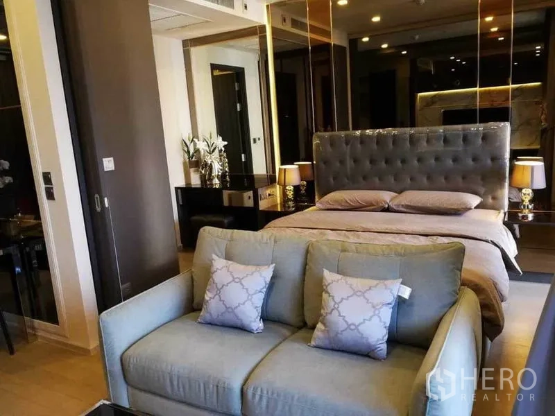 Condominium for rent in Watthana, Bangkok - Open-plan layout with a tufted-headboard bed behind a compact sofa and mirrored walls.