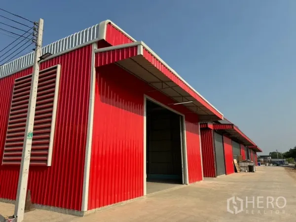 Warehouse for rent in Lam Luk Ka, Pathum Thani - Row of red and gray warehouse bays with side ventilation louvres along the access road.
