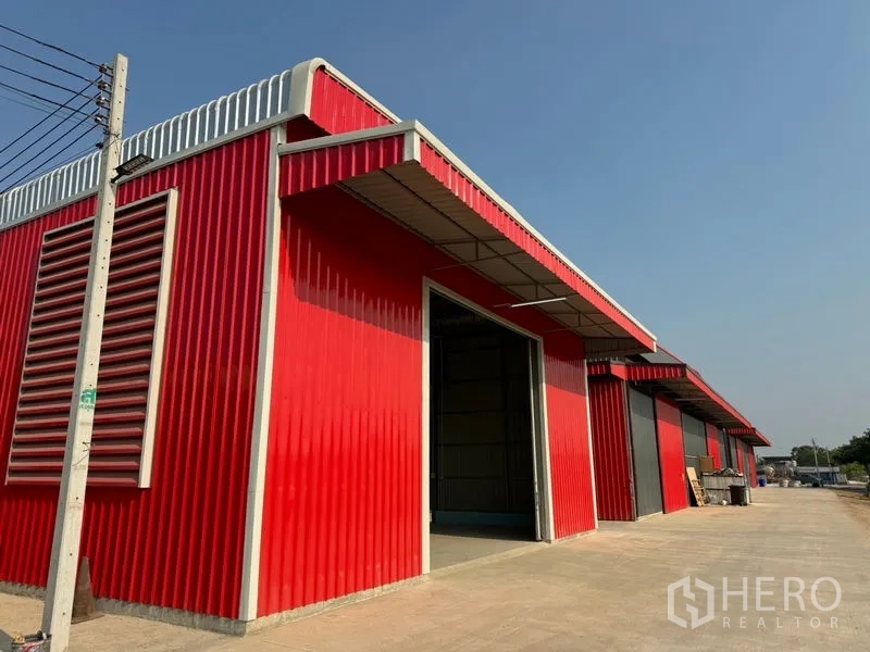 Warehouse for rent in Lam Luk Ka, Pathum Thani - Row of red and gray warehouse bays with side ventilation louvres along the access road.