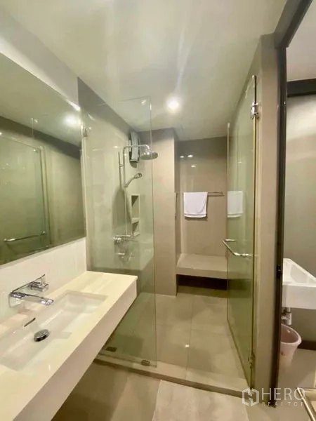 Condominium for rent in Khlong Toei, Bangkok - Contemporary bathroom with glass-enclosed shower, wide vanity and neutral tiles.