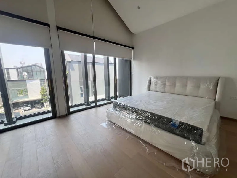 Townhouse for rent in Phra Khanong, Bangkok - Bright master bedroom with floor-to-ceiling windows and wood floors in a Phra Khanong townhouse.