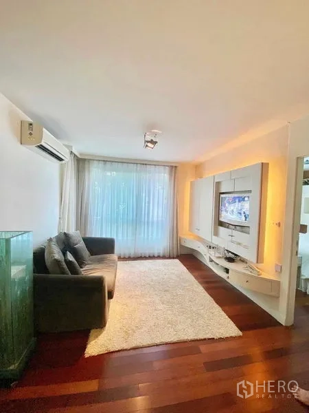 Condominium for rent in Watthana, Bangkok - Cozy living room with sofa, media wall, area rug, and large window with sheer curtains.