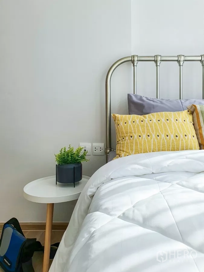 Condominium for rent in Khlong Toei, Bangkok - Detail of bed with yellow cushion and white duvet beside small plant.