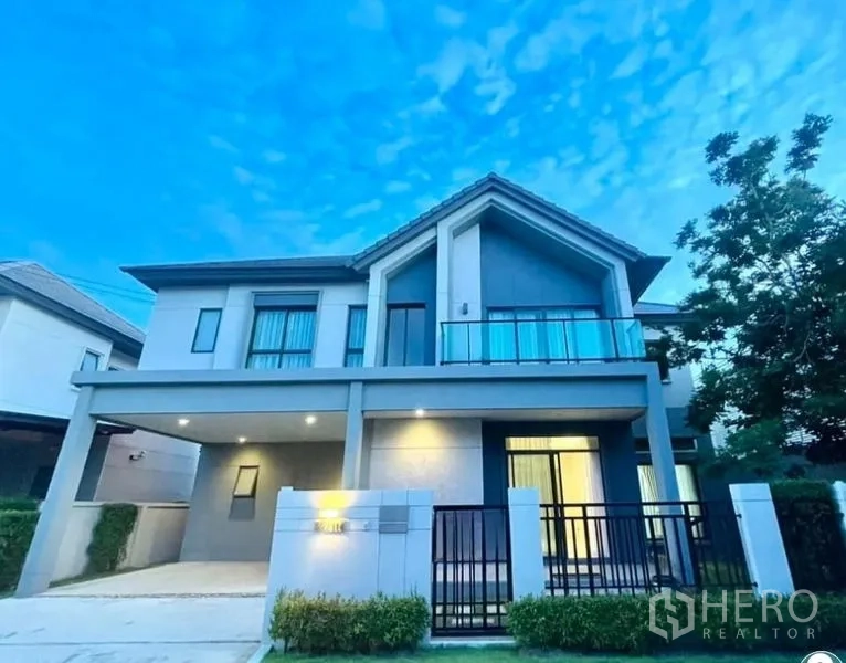Detached House for sale in Bang Kruai, Nonthaburi - Modern two‑storey detached house with gated fence, covered carport and glass‑railed balcony at dusk.