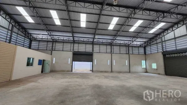 货栈 出租在Chon Buri - 仓库内景再现，高挑屋顶与中央卷帘门。