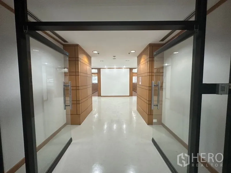 办公空间 出租在Phaya Thai, Bangkok - 玻璃双开门通向明亮走廊，木质墙面与射灯相衬的办公入口。
