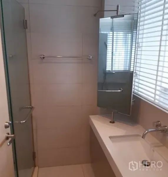 Condominium for rent in Khlong Toei, Bangkok - Clean bathroom featuring a glass-enclosed shower, long vanity countertop, wall mirror and window blinds.