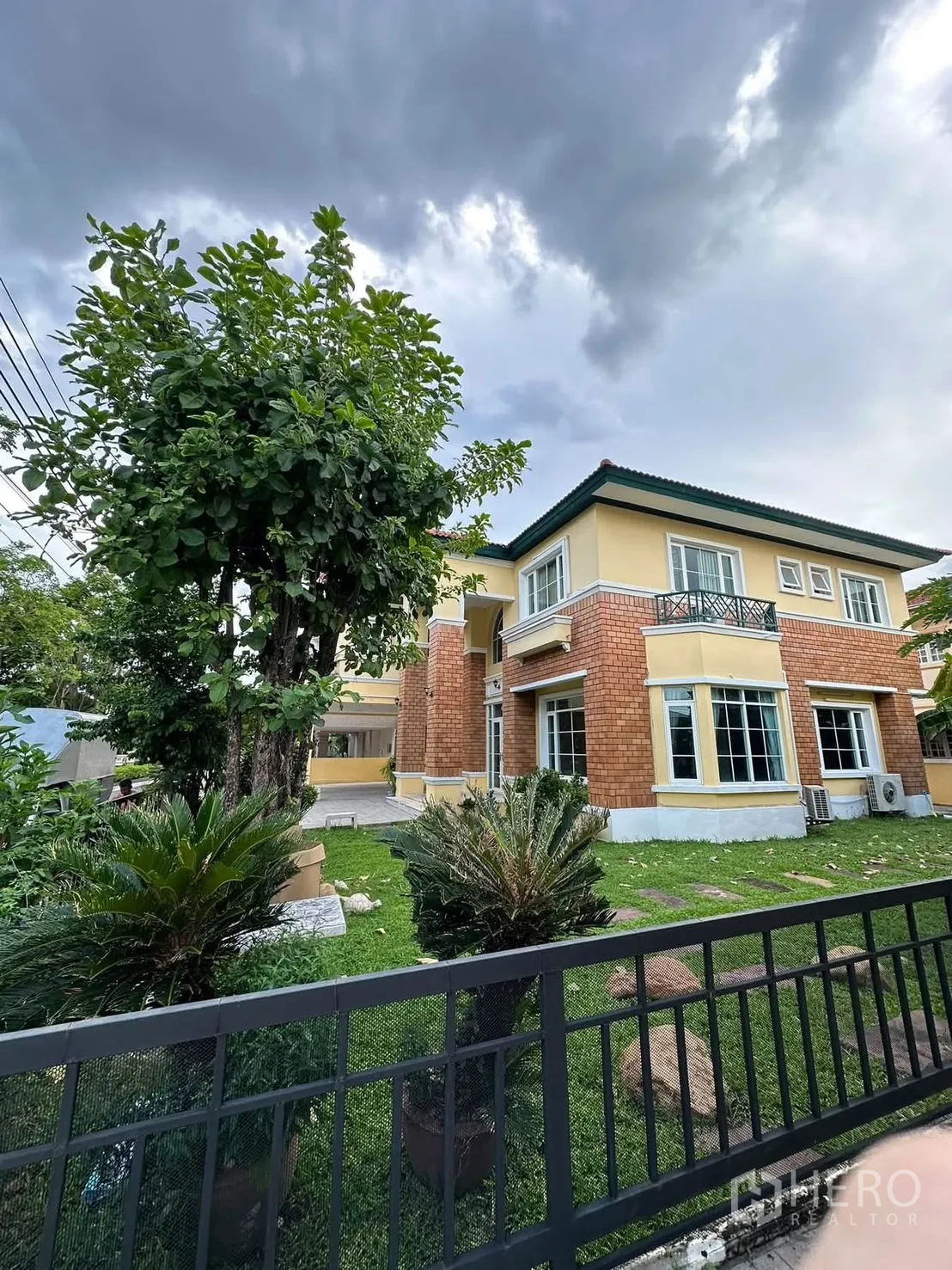 Detached House for rent in Phra Khanong, Bangkok - Side garden with lawn, mature trees, potted plants, and a fence alongside the house.
