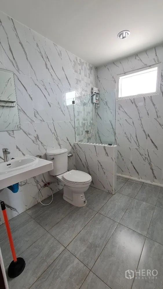 Detached House for rent in Lat Phrao, Bangkok - Bathroom with marble-effect tiles, toilet, sink and walk-in shower with glass screen.