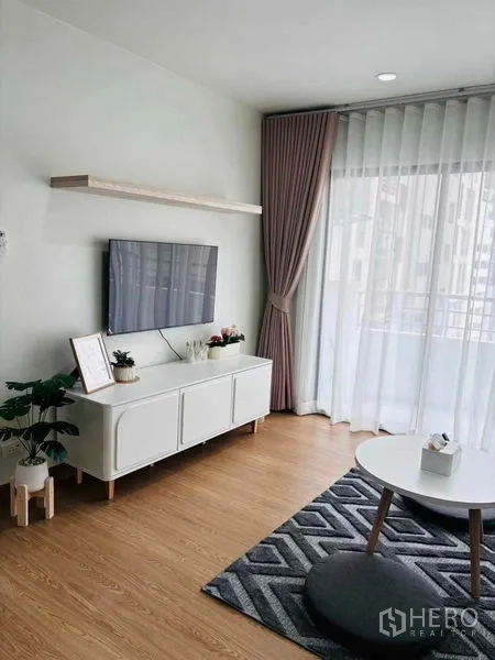 Shophouse for rent in Watthana, Bangkok - Living room with TV console, potted plants and full-height drapes leading to the balcony.