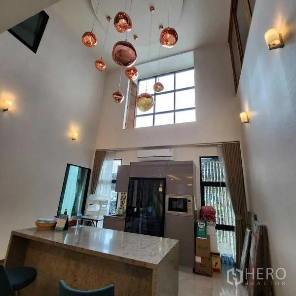 独立式住宅 出售在Phra Khanong, Bangkok - 挑高厨房，大型岛台、落地窗与铜色吊灯
