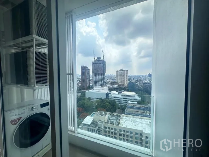 Condominium for rent - Utility balcony with washer-dryer and AC units beside a tall window framing the Bangkok skyline.