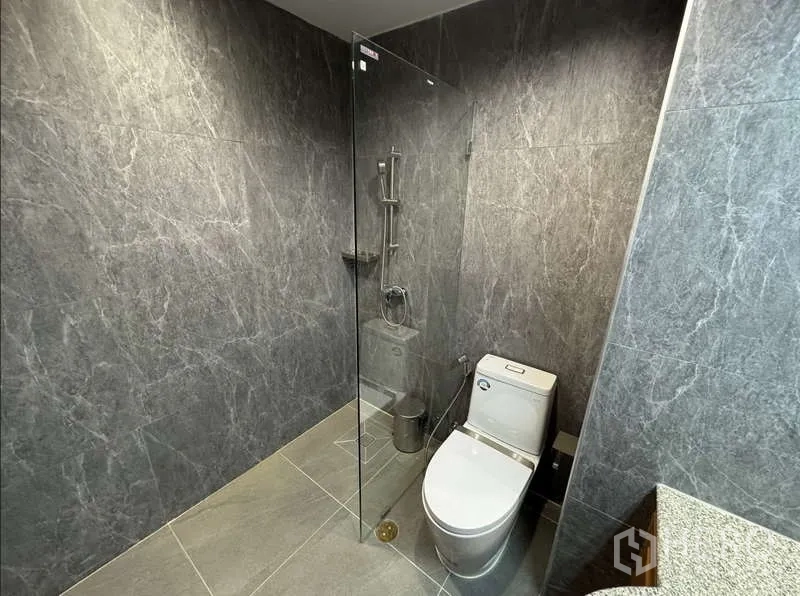Condominium for rent - Guest bathroom with glass-enclosed shower and toilet set against gray tiles.