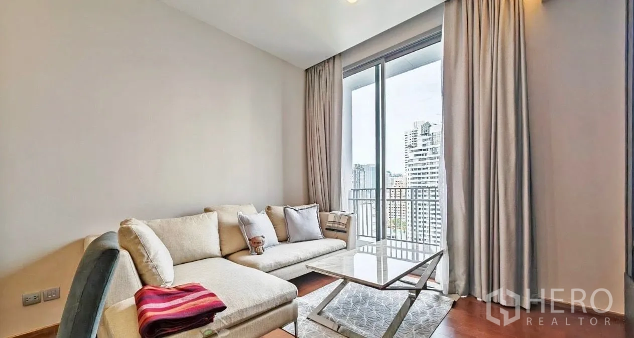 公寓 出租在Watthana, Bangkok - 明亮的客厅转角，米色沙发、石材茶几，落地窗通往阳台，享城市景观。