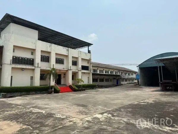 工厂 出租或出售在Bang Phli, Samut Prakan - 两层厂房办公楼，红色台阶，前方宽阔混凝土院场与带顶仓库。