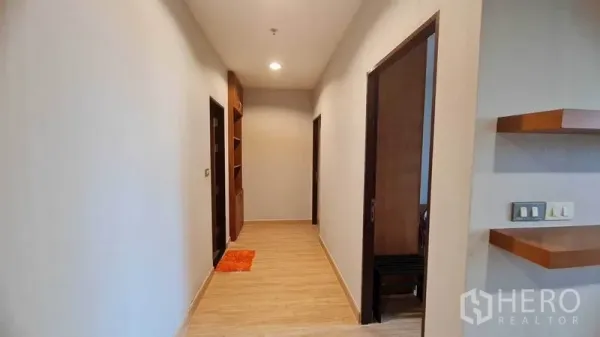 公寓 出租或出售在Watthana, Bangkok - 明亮走廊，木地板与嵌灯，两侧为卧室与浴室，尽头有嵌入式书架。