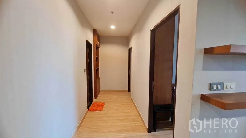 公寓 出租或出售在Watthana, Bangkok - 明亮走廊，木地板与嵌灯，两侧为卧室与浴室，尽头有嵌入式书架。