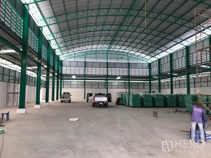 Factory for rent or sale in Mueang Samut Sakhon, Samut Sakhon - Open production area with vehicles and stacked materials under an arched roof.