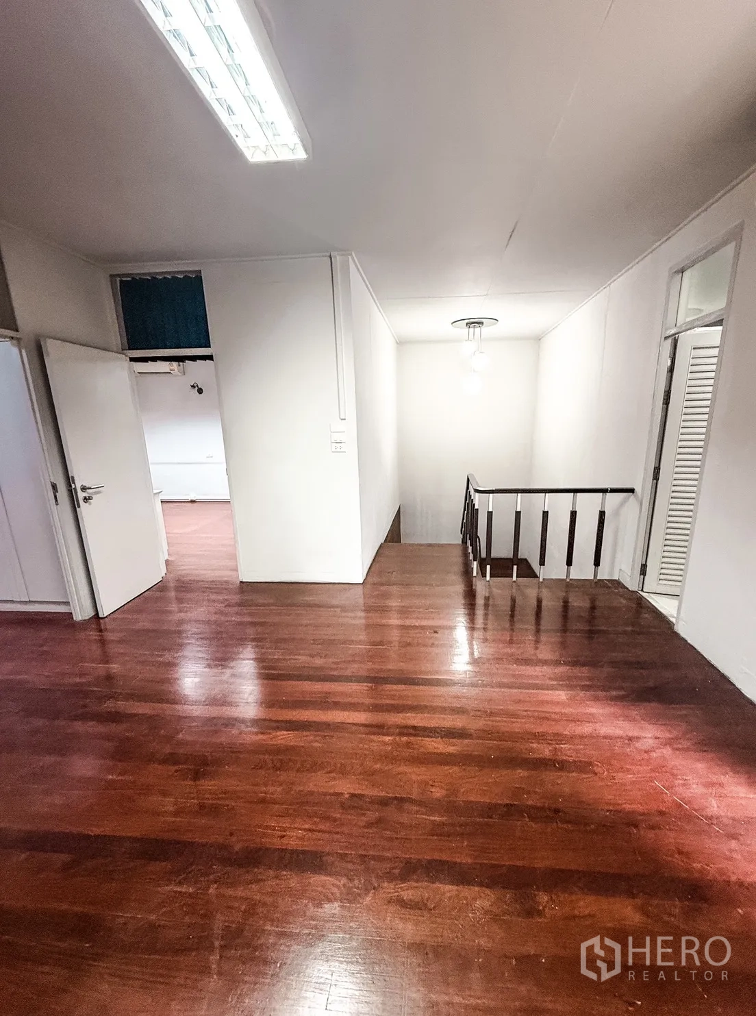 家庭办公室 for rent in Watthana, Bangkok - 二层平台区，亮光木地板通向楼梯与相邻房间，顶部长条灯照明。