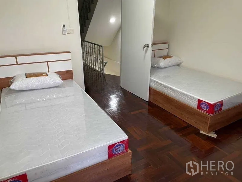 带办公室的家 出租或出售在Watthana, Bangkok - 靠近楼梯的双单人床卧室，拼花地板与白墙。