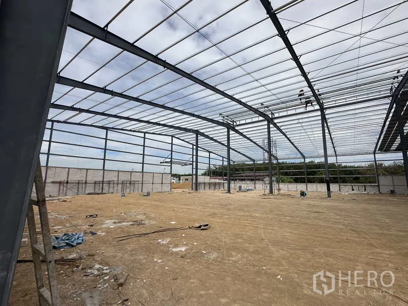 货栈 出租或出售在Nikhom Phatthana, Rayong - 高净空钢结构仓库内部斜角视图，四周设有围墙。