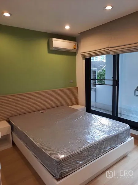 Condominium for rent in Watthana, Bangkok - Second bedroom with green accent wall, air conditioner and sliding door opening to the balcony.