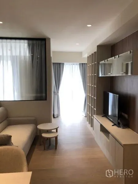 公寓 出租在Watthana, Bangkok - 曼谷瓦塔那区一居室公寓客厅，定制电视墙与置物架，落地窗通往阳台