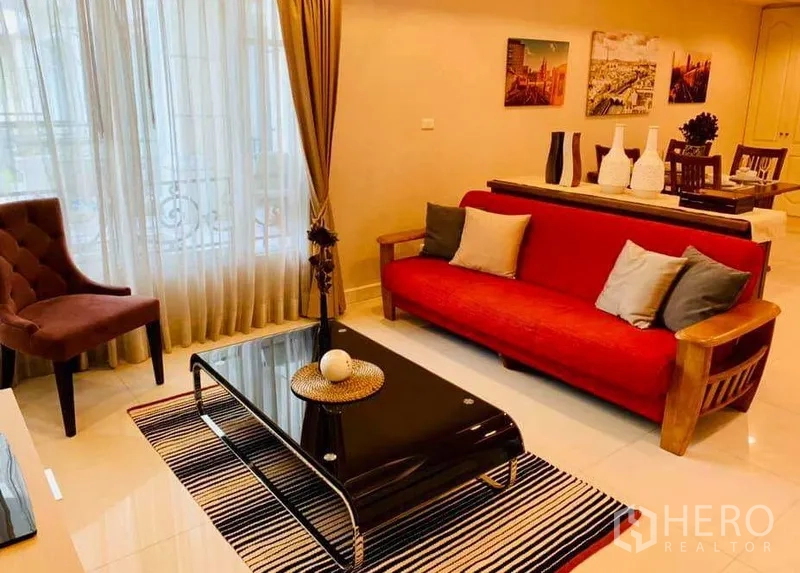 Condominium for rent in Khlong Toei, Bangkok - Open-plan living and dining area with red sofa, glass coffee table and balcony doorway.