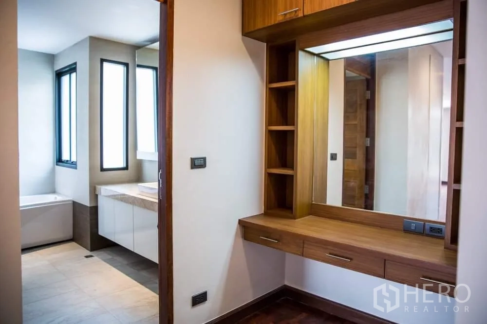 Detached House for rent in Khlong Toei, Bangkok - Built-in wooden vanity with shelving next to a modern bathroom with windows.