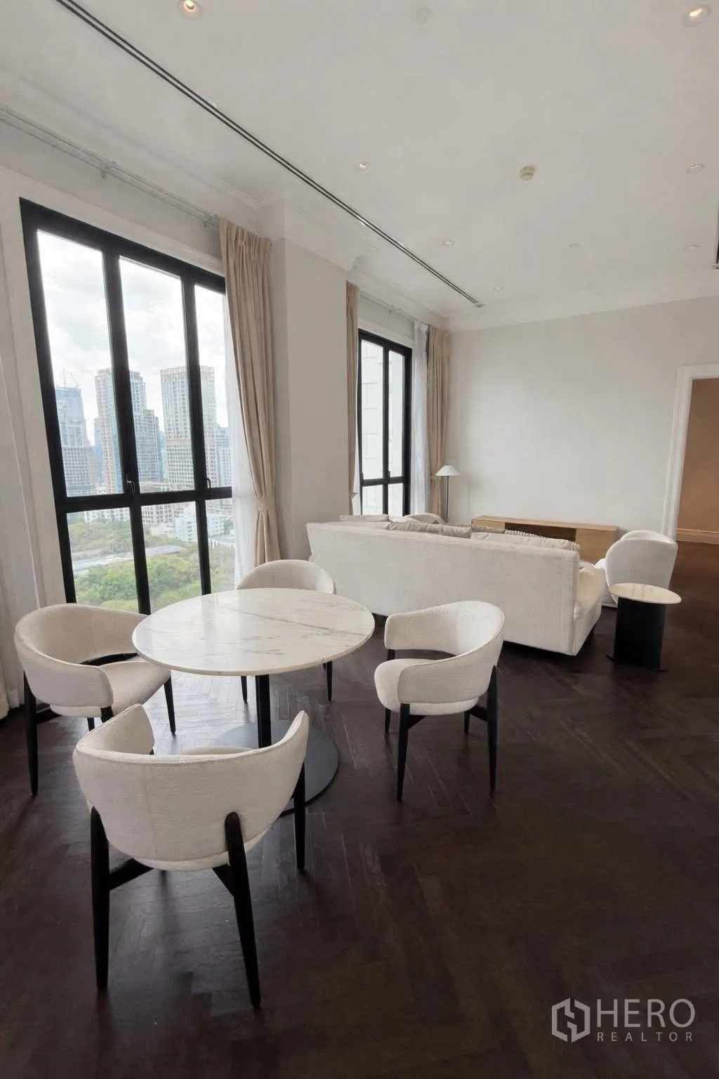 คอนโด for rent or sale in Pathum Wan, Bangkok - พื้นที่นั่งเล่นและรับประทานอาหารพร้อมโต๊ะหินอ่อนทรงกลม โซฟา และวิวสกายไลน์ผ่านหน้าต่างสูง