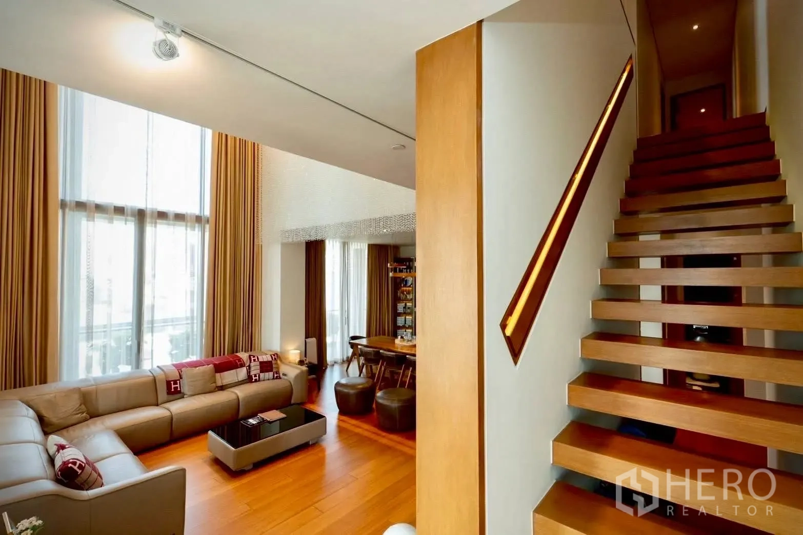 公寓 for sale in Sathon, Bangkok - 挑高客厅配L型沙发与漂浮式木楼梯。