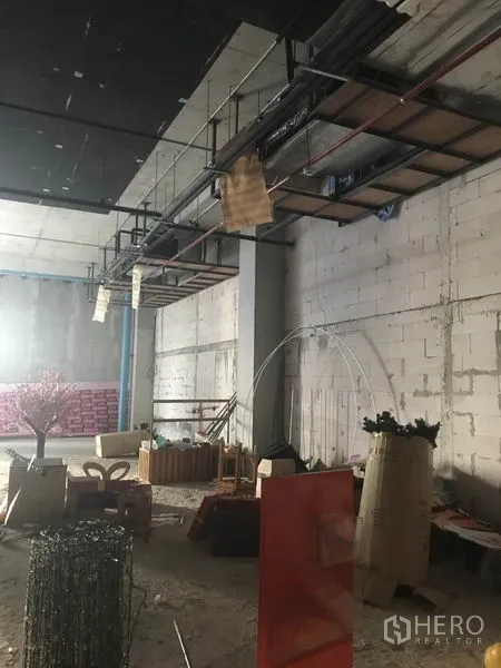 Retail Space for rent in Khlong Toei, Bangkok - Unfinished retail interior with high ceiling, exposed piping and block walls, with materials on the floor.