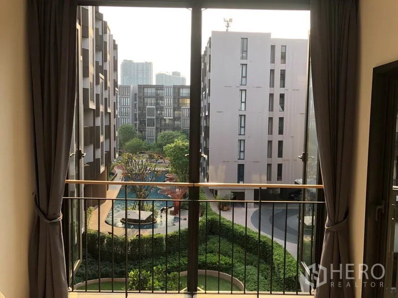 Condominium for rent in Watthana, Bangkok - Balcony view of low-rise buildings, lush gardens, and a free-form swimming pool.