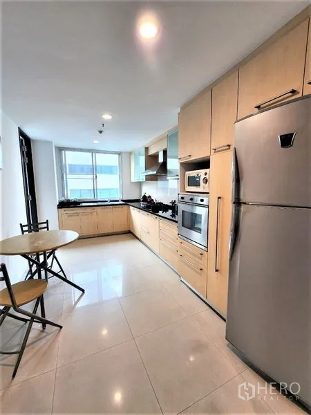 Condominium for rent in Bang Rak, Bangkok - Enclosed modern kitchen with light wood cabinetry, built-in oven, stainless refrigerator, range hood and breakfast nook by the window.
