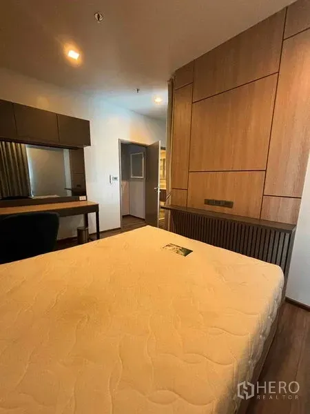 Condominium for rent or sale in Watthana, Bangkok - Bedroom featuring wood panel wall, long desk and warm lighting near the doorway.