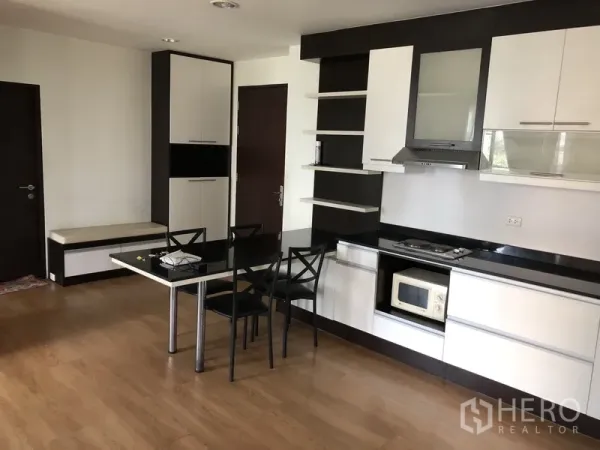 公寓 出租在Khlong Toei, Bangkok - 开放式厨房，白色橱柜与黑色台面，电炉与餐桌，木地板。