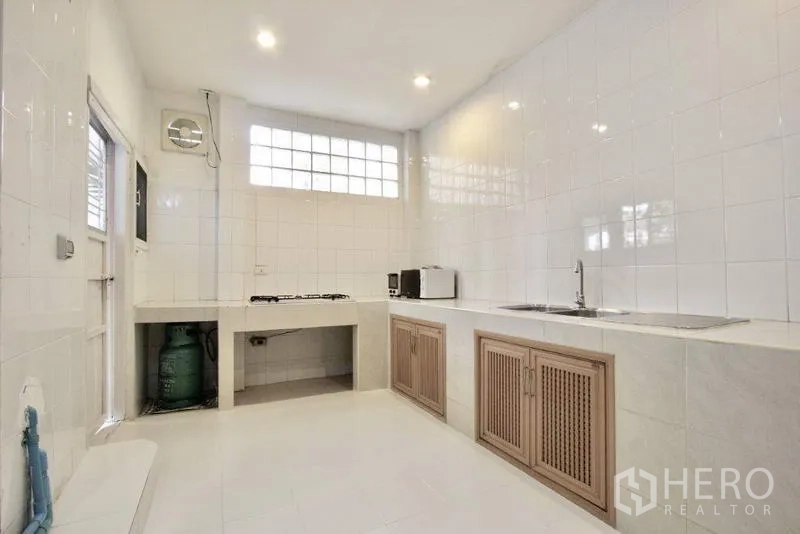 Townhouse for sale in Suan Luang, Bangkok - Spacious white-tiled Thai kitchen with gas hob, sink, and storage cabinets.