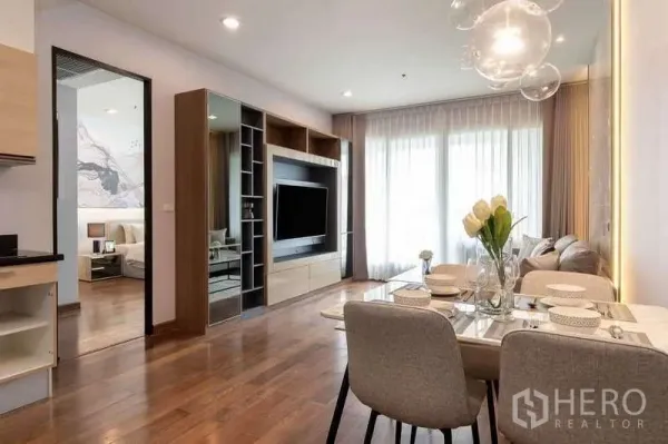 Condominium for rent in Pathum Wan, Bangkok - Open-plan living and dining area with built-in TV wall, wood floors, and floor-to-ceiling curtains.
