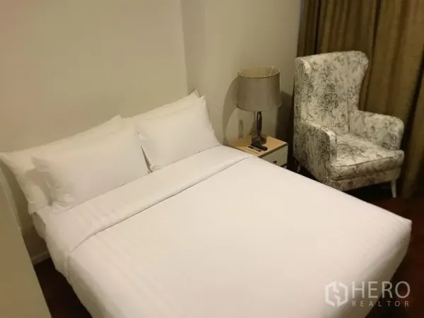 Condominium for rent in Watthana, Bangkok - Cozy bedroom with double bed, bedside table and lamp, plus a patterned armchair.