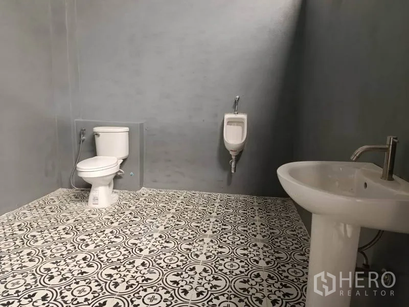 Warehouse for rent in Saphan Sung, Bangkok - Clean restroom inside the warehouse with patterned tile floor, toilet, urinal, and pedestal sink.
