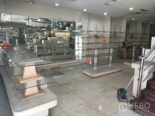 Shophouse for rent in Watthana, Bangkok - Ground-floor retail space with glass display shelves, mirrored wall, tiled floor and staircase.