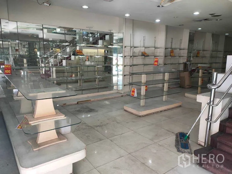 Shophouse for rent in Watthana, Bangkok - Ground-floor retail space with glass display shelves, mirrored wall, tiled floor and staircase.