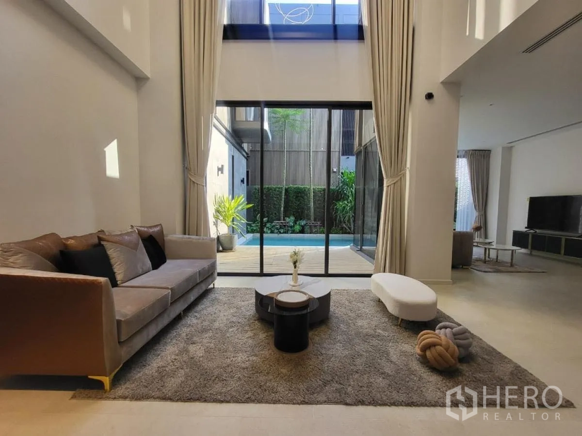 Detached House for rent in Wang Thonglang, Bangkok - High-ceiling lounge with tall curtains and glass doors overlooking the courtyard pool.