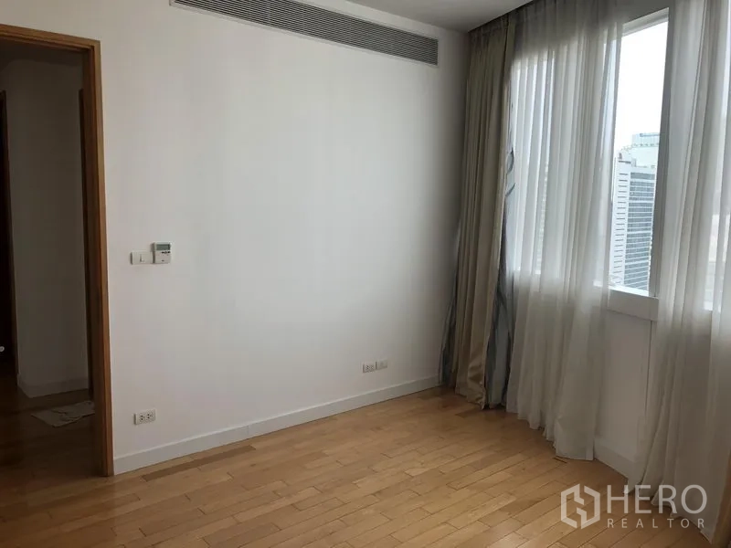 Condominium for rent in Khlong Toei, Bangkok - Bedroom with city-view windows, sheer curtains and light wood floors.