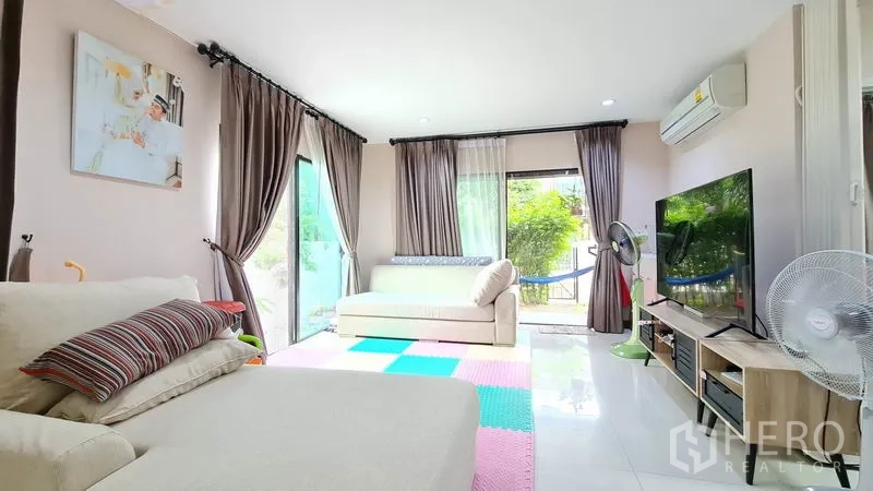 Detached House for sale in Samut Prakan - Bright living room with sofas, sliding glass doors and garden views.