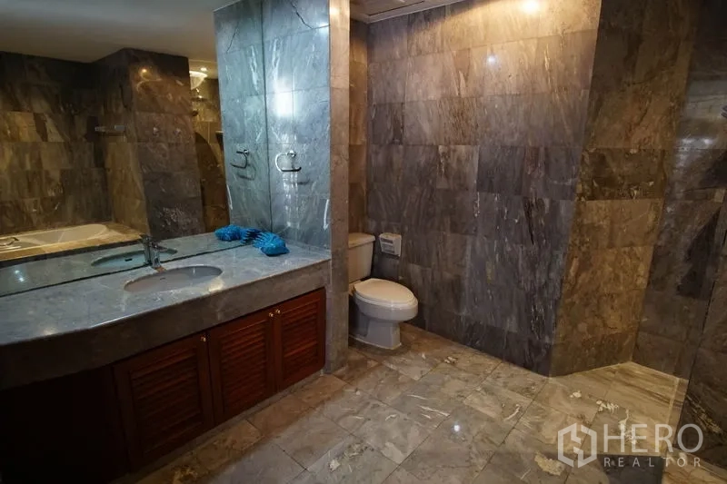 Apartment for rent in Watthana, Bangkok - Expansive bathroom with marble vanity, wide mirror, toilet, and walk-in shower area.