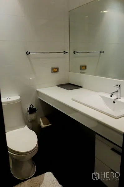 Condominium for sale in Watthana, Bangkok - Modern bathroom with white vanity, wide mirror and toilet.